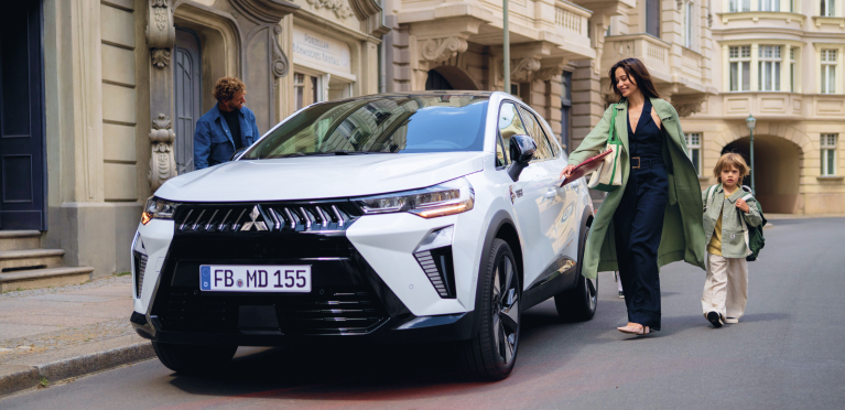 Eine Vierköpfige Familie läuft auf den parkenden Grandis zu.