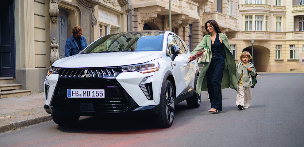 Eine Vierköpfige Familie läuft auf den parkenden Grandis zu.