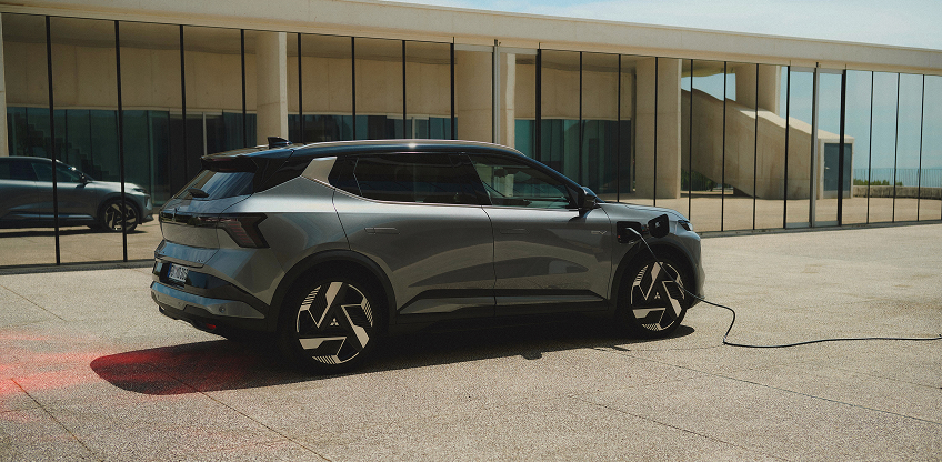 Der Mitsubishi Eclipse Cross Ein grauer Mitsubishi Eclipse Cross steht mit eingestecktem Ladekabel vor einer Galerie.