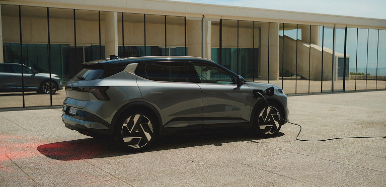 Der Mitsubishi Eclipse Cross Ein grauer Mitsubishi Eclipse Cross steht mit eingestecktem Ladekabel vor einer Galerie.