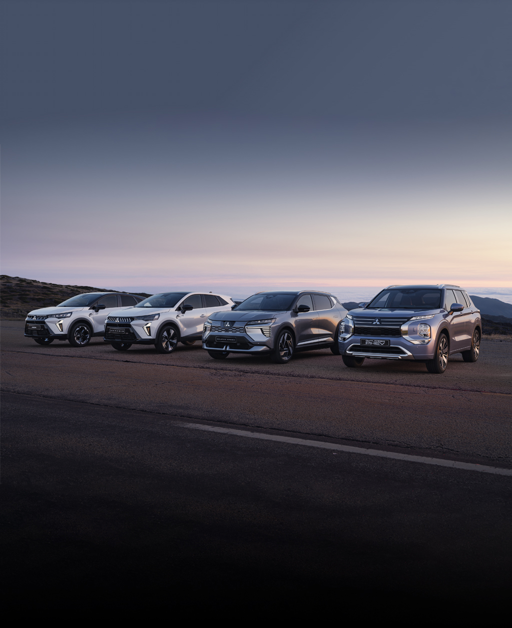 Die Mitsubishi Modell-Range Die Mitsubishi ASX, Grandis, Eclipse Cross und Outlander stehen in der Dämmerung am Straßenrand.