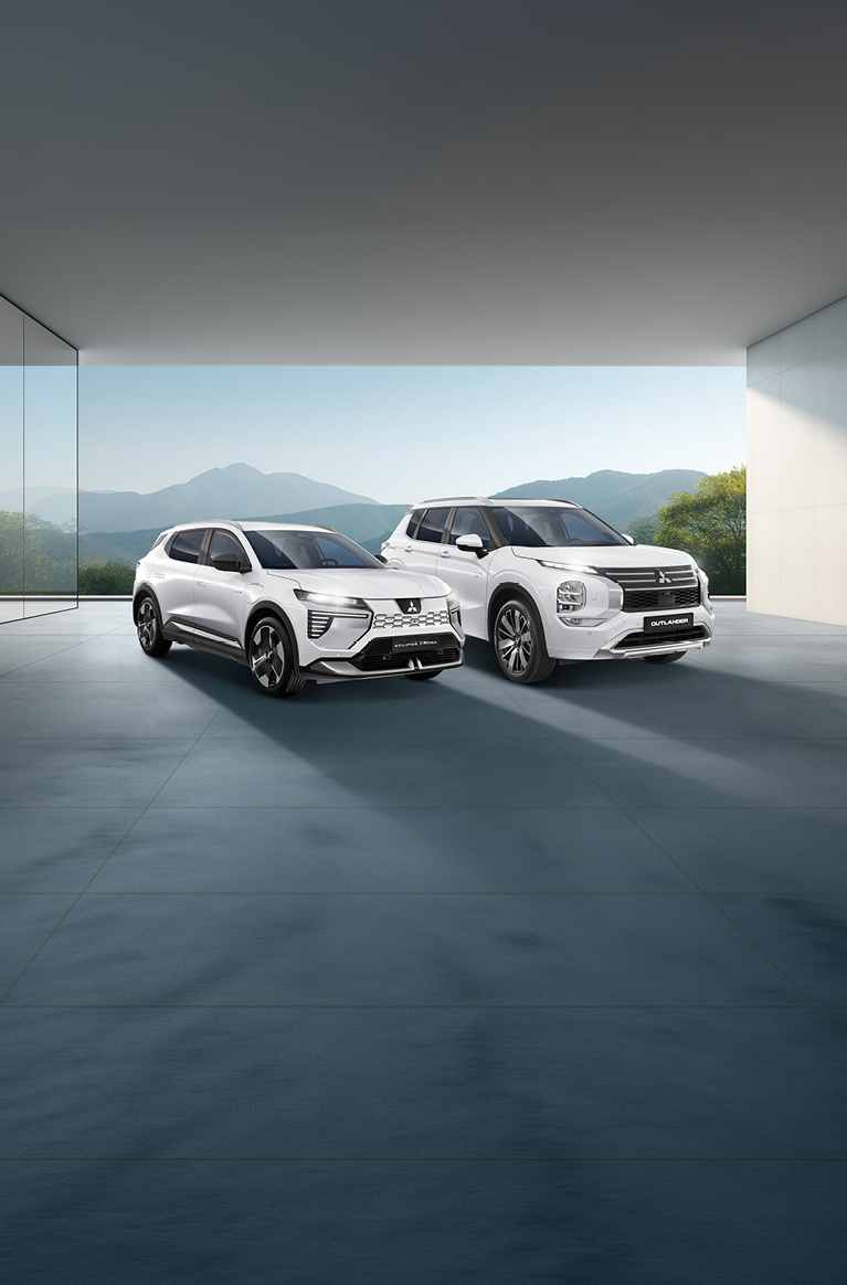MITSUBISHI MOTORS Elektromobilität Zwei weiße Mitsubishi-SUVs - ein Outlander und ein Eclipse Cross - stehen nebeneinander in einem modernen, lichtdurchfluteten Showroom mit Blick auf eine Berglandschaft.