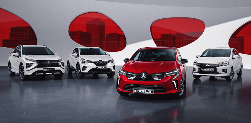 Ein weisser Eclipse Cross, ein weisser ASX, ein roter COLT und ein weisser Space Star stehen aufgereiht vor einer wei&szlig;en Wand mit roten runden Fenstern.