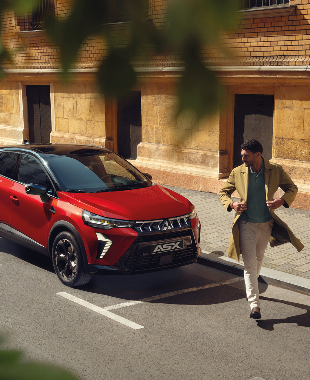 Roter Mitsubishi ASX Kompakt-SUV parkt in der Stadt, Front- und Seitenansicht; vor dem Fahrzeug &uuml;berquert ein Mann in beigem Mantel die Stra&szlig;e.