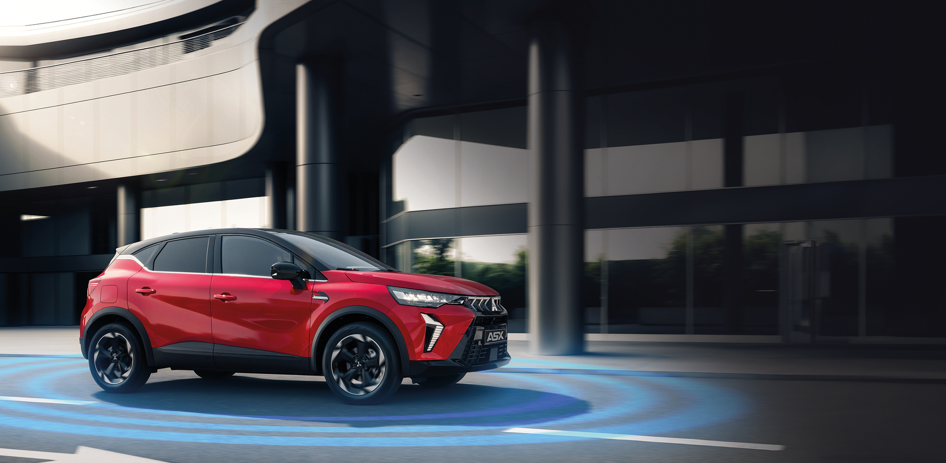 Roter Mitsubishi ASX f&auml;hrt vor einer modernen Geb&auml;udefassade, um das Fahrzeug sind blaue, kreisf&ouml;rmige Linien als Symbol f&uuml;r aktive Sicherheits  und Fahrerassistenzsysteme wie Abstands  und Spurhalteassistent eingeblendet.