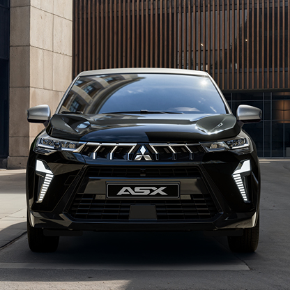 Frontansicht eines Mitsubishi ASX Black, der in einer modernen Stadtpassage mit hohen Geb&auml;uden und Holzfassade steht; das Bild hebt den markanten K&uuml;hlergrill, die LED Signatur und den hochwertigen Auftritt des Sondermodells hervor.