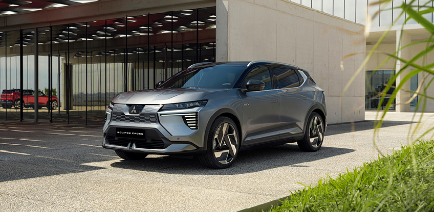 Der graue Mitsubishi Eclipse Cross steht vor einem modernen Geb&auml;ude in Dreiviertel-Frontalperspektive und zeigt seine robuste Front sowie die markanten LED-Leuchten.