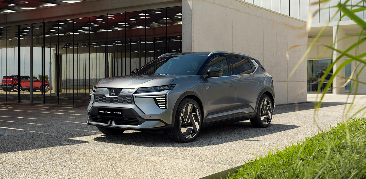 Der graue Mitsubishi Eclipse Cross steht vor einem modernen Geb&auml;ude in Dreiviertel-Frontalperspektive und zeigt seine robuste Front sowie die markanten LED-Leuchten.