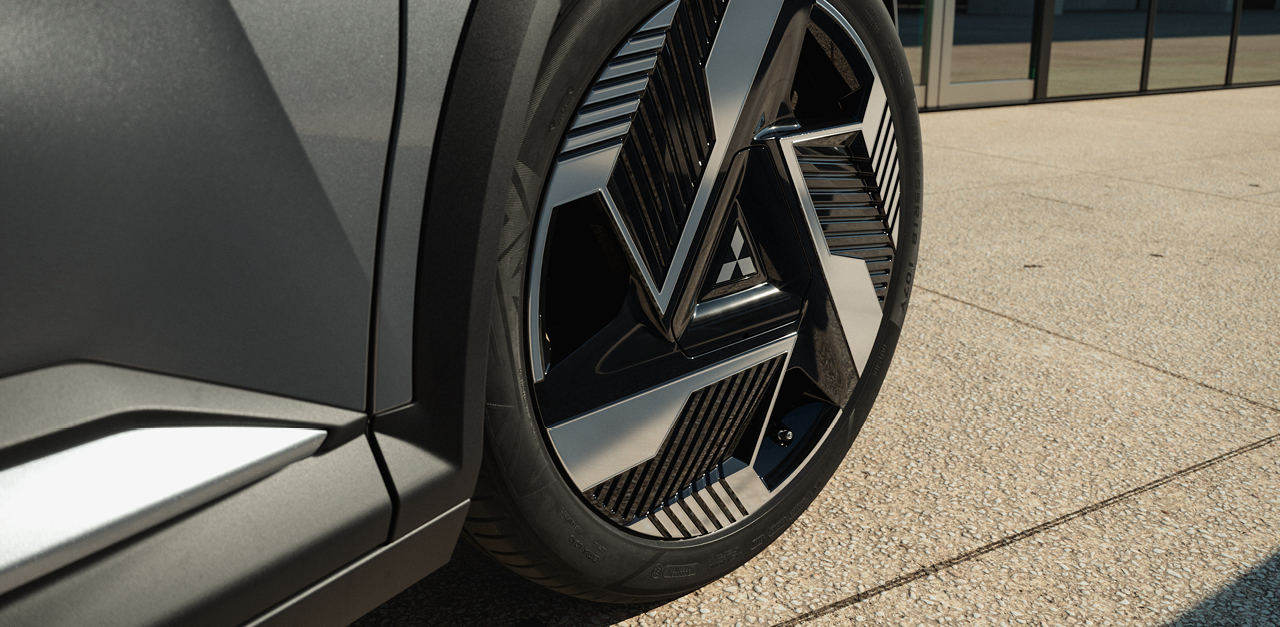 Ein grauer Mitsubishi Eclipse Cross ist aus der Heckansicht vor einem modernen Geb&auml;ude mit Fensterfront zu sehen.