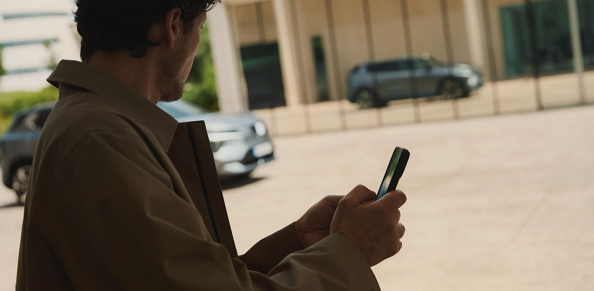 MITSUBISHI CONNECT App Mann mit Handy in der Hand betrachtet den vorbeifahrenden Eclipse Cross