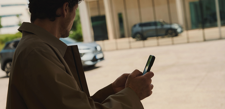 MITSUBISHI CONNECT App Mann mit Handy in der Hand betrachtet den vorbeifahrenden Eclipse Cross