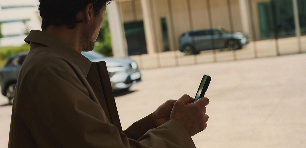 MITSUBISHI CONNECT App Mann mit Handy in der Hand betrachtet den vorbeifahrenden Eclipse Cross