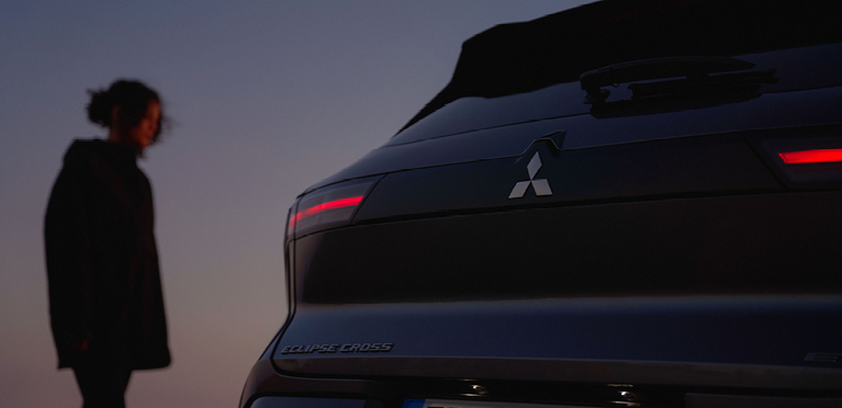 Eine Frau betrachtet das Heck des neuen Mitsubishi Eclipse Cross in der Dämmerung.