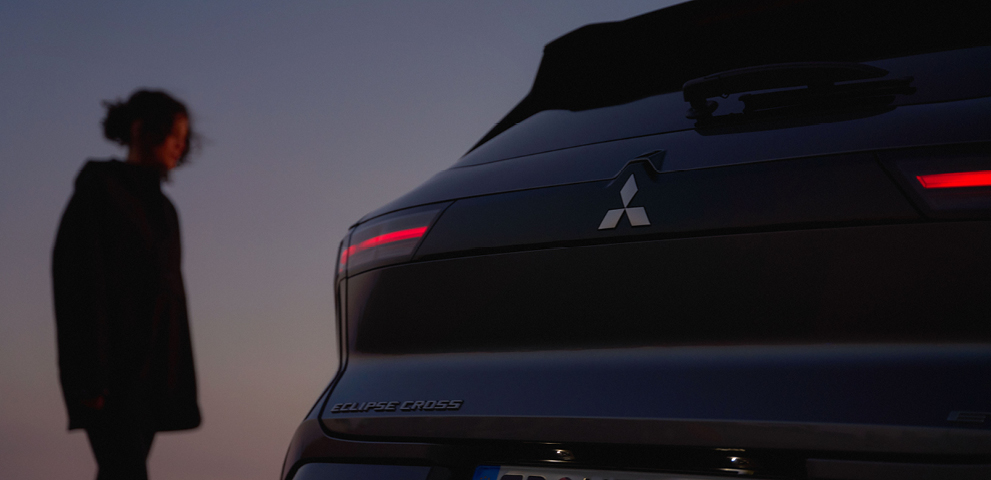 Eine Frau betrachtet das Heck des neuen Mitsubishi Eclipse Cross in der Dämmerung.