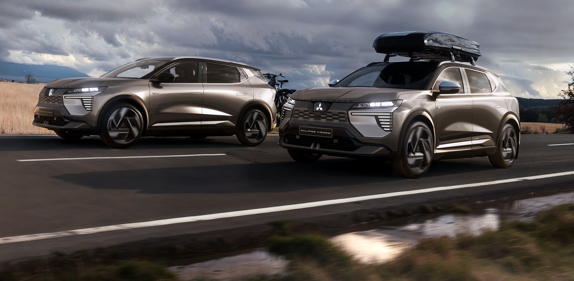 Zwei Mitsubishi Eclipse Cross, einer mit Fahrrad-Hecktr&auml;ger, einer mit Dachbox, fahren eine Landstra&szlig;e entlang.