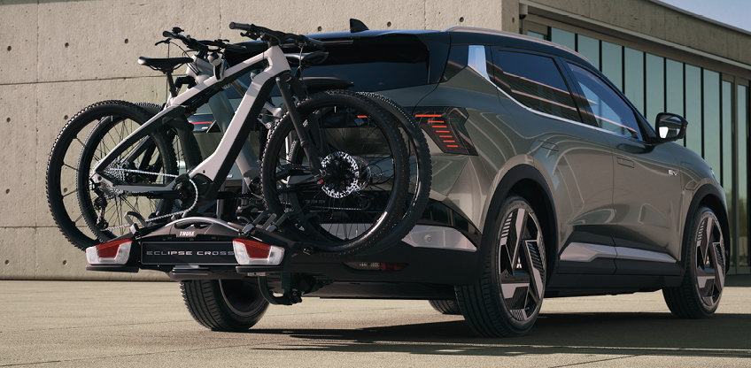 Der Mitsubishi Eclipse Cross mit Fahrrad-Hecktr&auml;ger, beladen mit 2 Fahrr&auml;dern, steht vor einem modernen Geb&auml;ude.