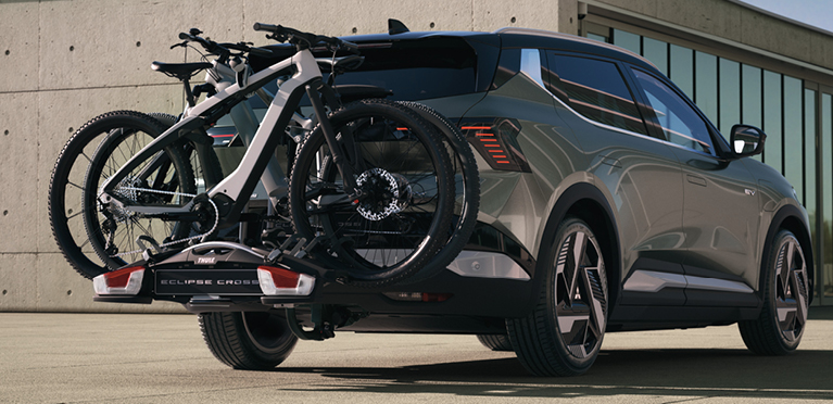 Der Mitsubishi Eclipse Cross mit Fahrrad-Hecktr&auml;ger, beladen mit 2 Fahrr&auml;dern, steht vor einem modernen Geb&auml;ude.