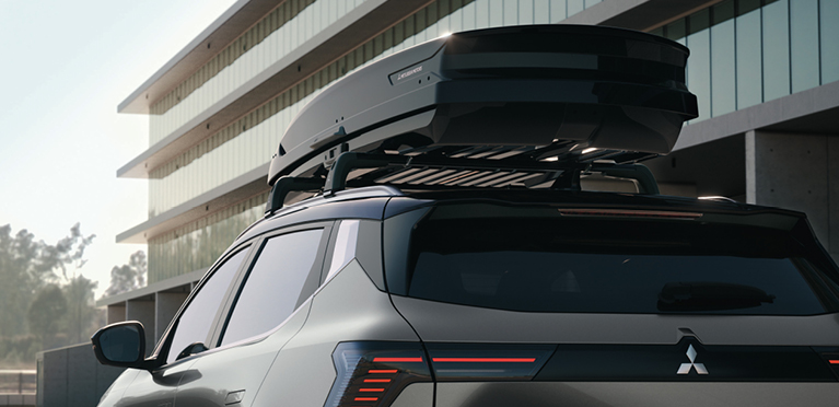 Der Mitsubishi Eclipse Cross mit einer Dachbox vor einem modernen Geb&auml;ude.