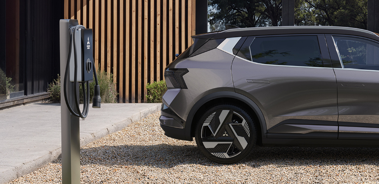 Ein geparkter Mitsubishi Eclipse Cross steht seitlich vor einem modernen Geb&auml;ude und ist neben einer freistehenden Wallbox Ladestation positioniert.