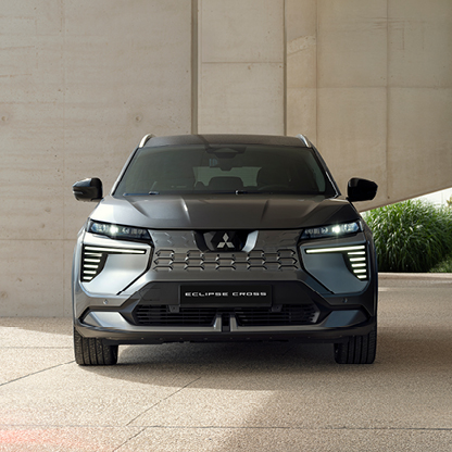 Mitsubishi Eclipse Cross Intro Edition von der Front Graue Mitsubishi Eclipse Cross Intro Edition steht frontal unter einer modernen Betonüberdachung; im Hintergrund sind eine begrünte Außenfläche und Tageslicht zu sehen.
