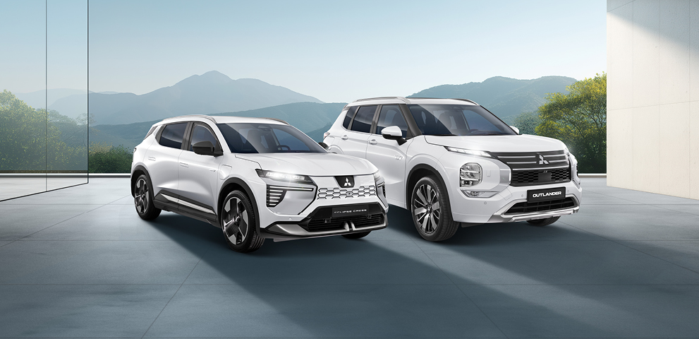 MITSUBISHI MOTORS Elektromobilität Zwei weiße Mitsubishi-SUVs - ein Outlander und ein Eclipse Cross - stehen nebeneinander in einem modernen, lichtdurchfluteten Showroom mit Blick auf eine Berglandschaft.