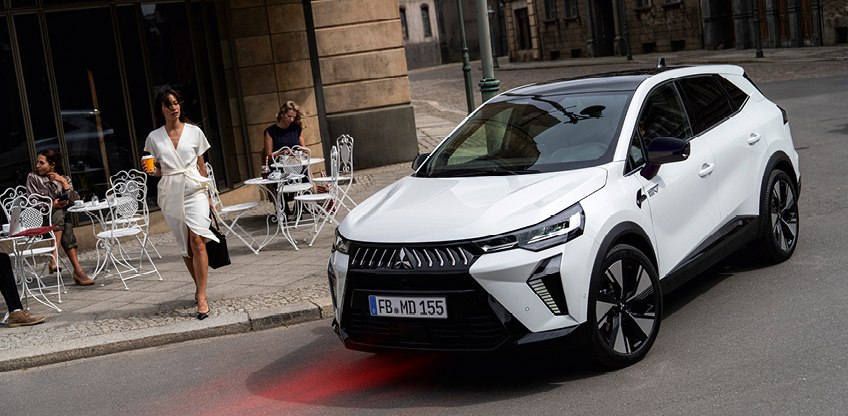 Wei&szlig;er Mitsubishi Grandis SUV in der Stadt vor einem Stra&szlig;encaf&eacute;, Frau in wei&szlig;em Kleid mit Kaffeebecher geht am Fahrzeug vorbei