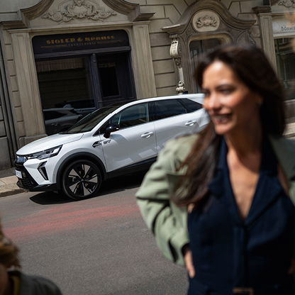 Wei&szlig;er Mitsubishi Grandis SUV vor einem historischen Stadtgeb&auml;ude, im unscharfen Vordergrund eine lachende Frau in Bewegung.
