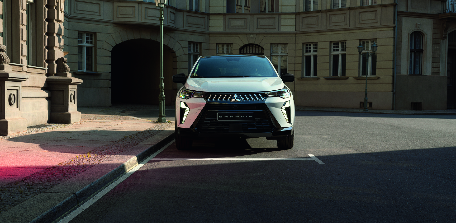 Mitsubishi Grandis – sichere Präsenz in der Stadt Weißer Mitsubishi Grandis steht frontal geparkt an einer ruhigen Stadtstraße vor einem historischen Gebäude.