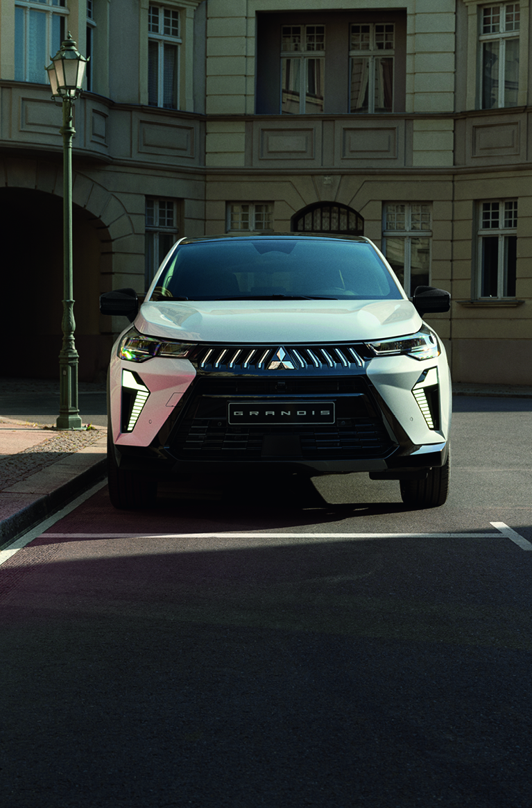 Mitsubishi Grandis – sichere Präsenz in der Stadt Weißer Mitsubishi Grandis steht frontal geparkt an einer ruhigen Stadtstraße vor einem historischen Gebäude.