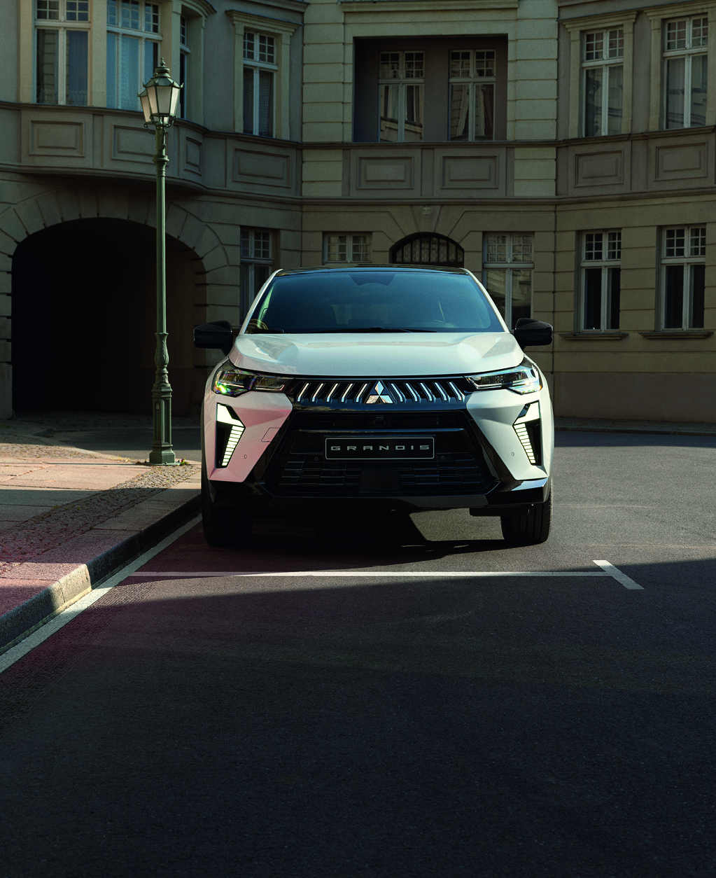 Mitsubishi Grandis – sichere Präsenz in der Stadt Weißer Mitsubishi Grandis steht frontal geparkt an einer ruhigen Stadtstraße vor einem historischen Gebäude.