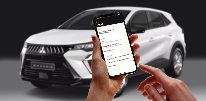 Eine Hand h&auml;lt ein Smartphone vor dunkelgrauem Hintergrund, w&auml;hrend die andere Hand kurz davor ist, den Bildschirm zu ber&uuml;hren. Auf dem Display ist das Icon Mitsubishi Motors App zu sehen.