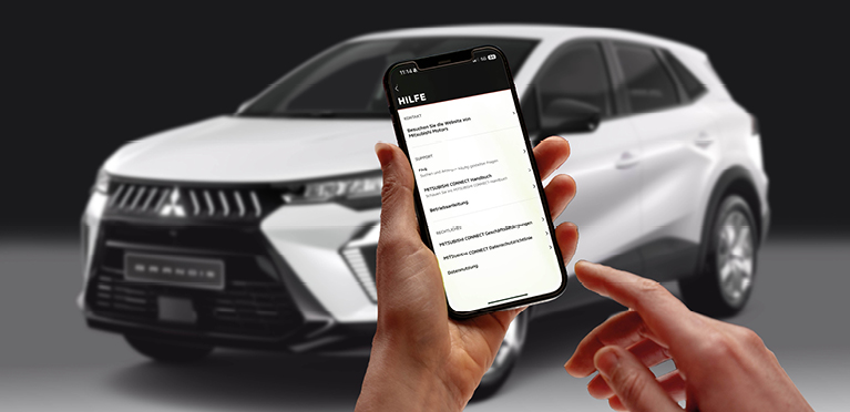 Eine Hand h&auml;lt ein Smartphone vor dunkelgrauem Hintergrund, w&auml;hrend die andere Hand kurz davor ist, den Bildschirm zu ber&uuml;hren. Auf dem Display ist das Icon Mitsubishi Motors App zu sehen.