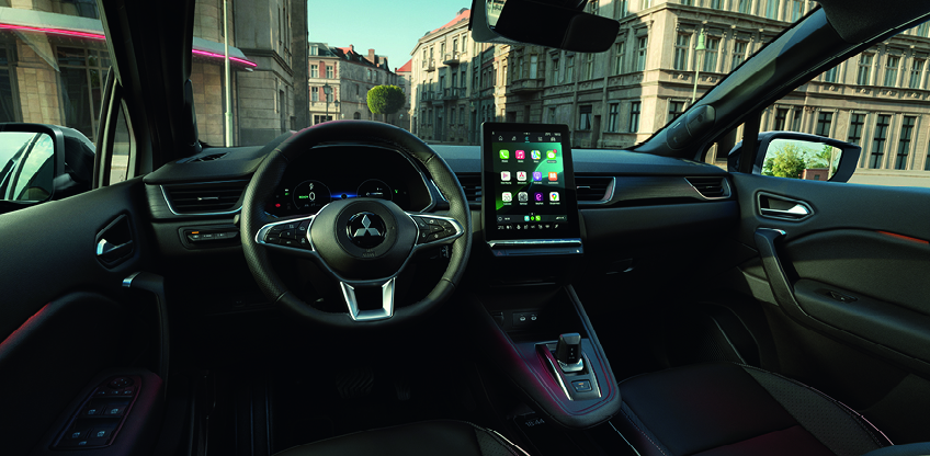 Modernen Innenraum eines Mitsubishi Grandis mit Multifunktionslenkrad, digitalem Cockpit und gro&szlig;em zentralen Touchscreen mit Apps, Blick nach au&szlig;en in eine Stadt.