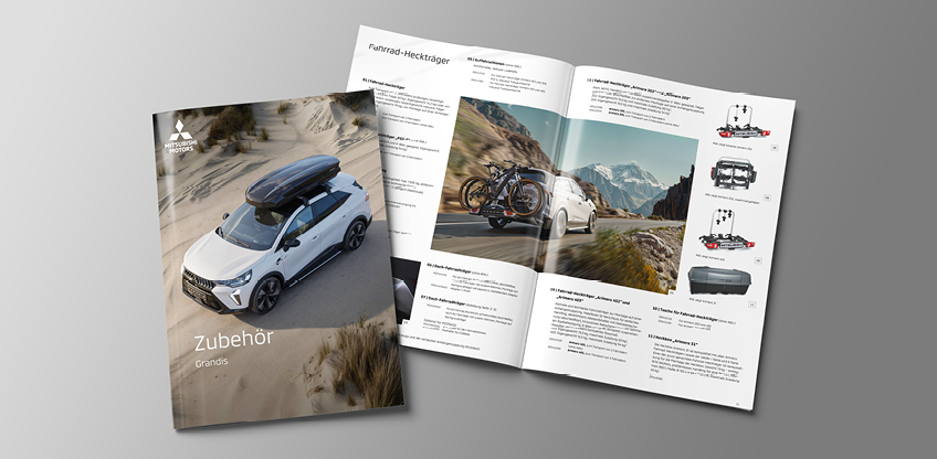 Geschlossene und ge&ouml;ffnete Zubeh&ouml;rbrosch&uuml;re f&uuml;r den Mitsubishi Grandis: Auf dem Titelbild f&auml;hrt das wei&szlig;e Fahrzeug mit montierter Dachbox durch eine sandige D&uuml;nenlandschaft. Die aufgeklappte Doppelseite zeigt Produktfotos und Beschreibungen von Autozubeh&ouml;r sowie ein gro&szlig;es Landschaftsbild mit einem Grandis auf einer Gebirgsstra&szlig;e und zwei Fahrr&auml;dern am Hecktr&auml;ger.