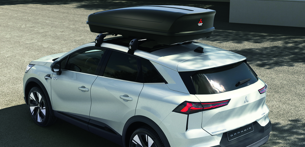 Wei&szlig;er Mitsubishi Grandis mit gro&szlig;er schwarzer Dachbox auf dem Dach, schr&auml;g von hinten oben aufgenommen.