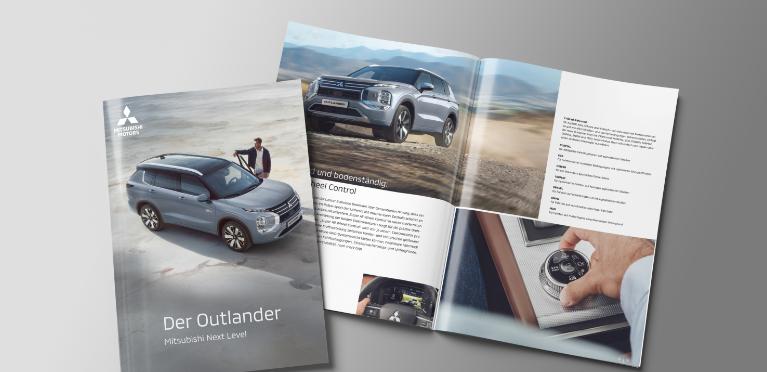 Die aufgeblätterte Broschüre des Outlander liegt auf grauem Untergrund.