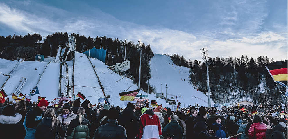 Mitsubishi ist Mobilitätspartner der Vierschanzentournee. Ein Skispringer mit daneben abgebildetem Logo von der Vierschanzentournee und Mitsubishi.